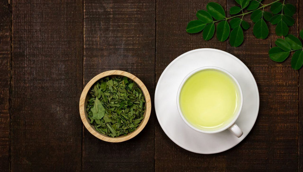 A white cup with Moringa tea and a small bowl with Moringa leaves.