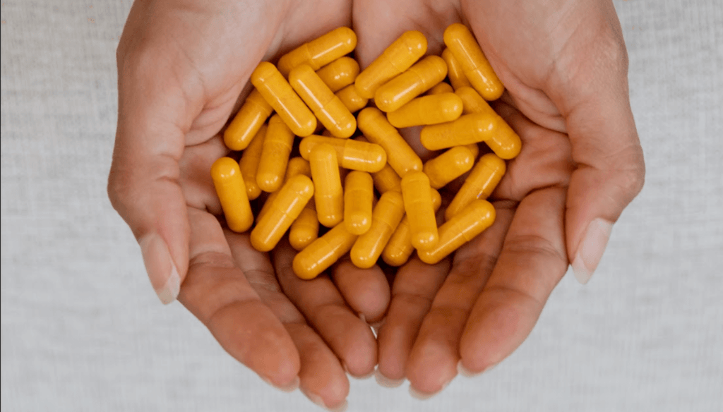 Two hands holding turmeric capsules