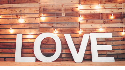 White letters spelling the word love in front of  wooden background with fairly lights