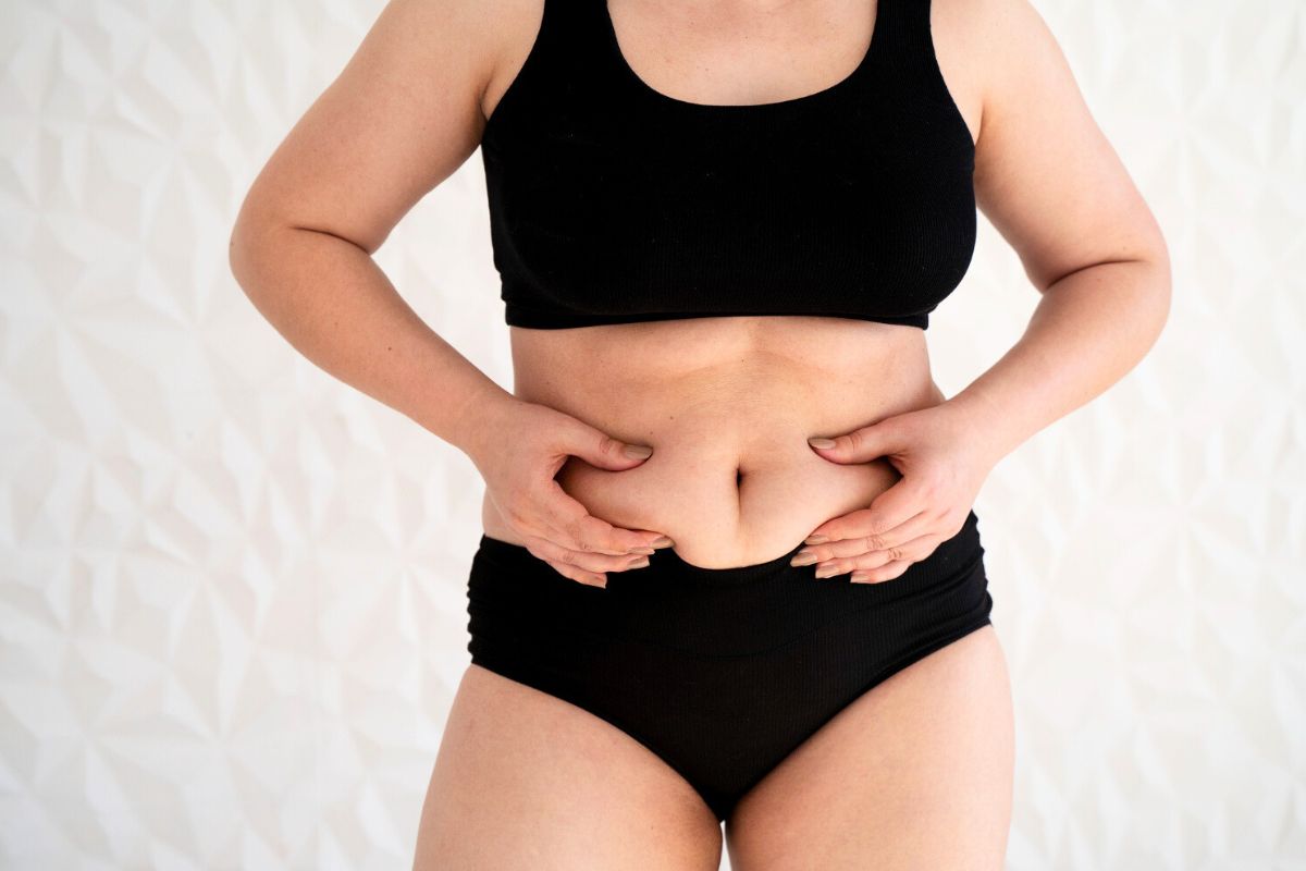 Mujer mirando su vientre después del parto, lo que ilustra los cambios físicos posparto