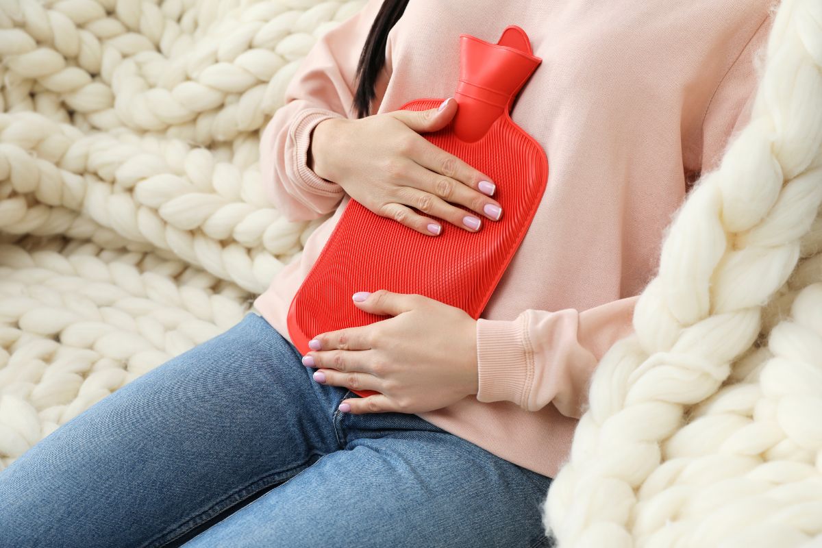 Femme utilisant une bouillotte chaude pour soulager les douleurs liées au retour de couches