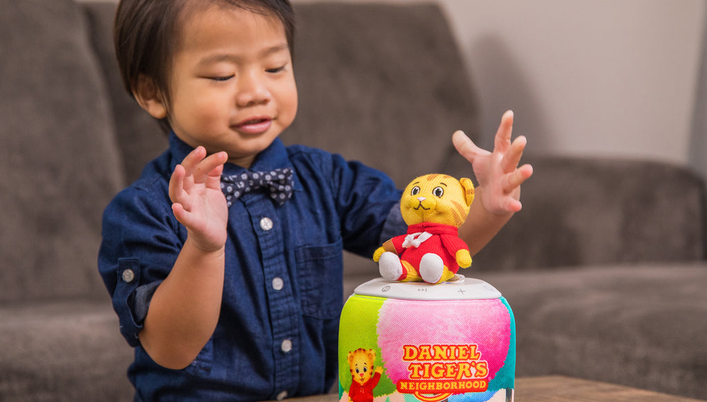 A smiling boy in a bowtie balances his Craftie atop his speaker as it tells him stories