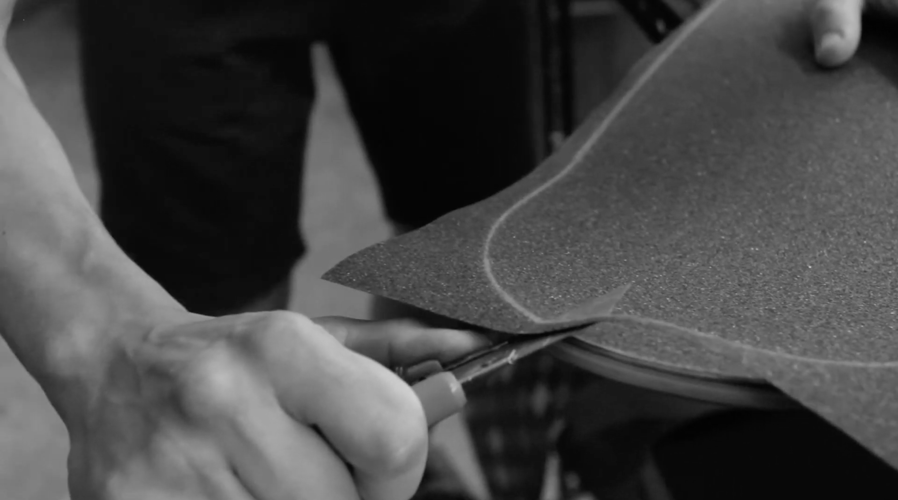 Using a sharp blade, cut the excess griptape from below, pulling the blade towards you and running against the deck edge
