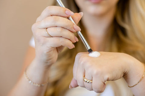 Tan background with a blonde woman swirling WinkClique cleanser on her makeup brush.