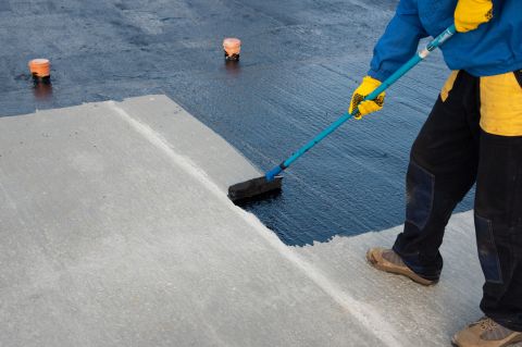 A worker rolling black bitumen paint onto concrete