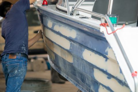 Sanding a repaired boat in preparation of applying marine paints for boats