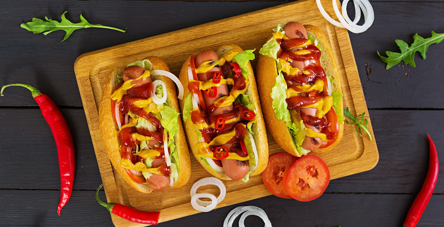 Three hot dogs with a heavy assortment of toppings such as ketchup, mustard, pickles, and coleslaw.