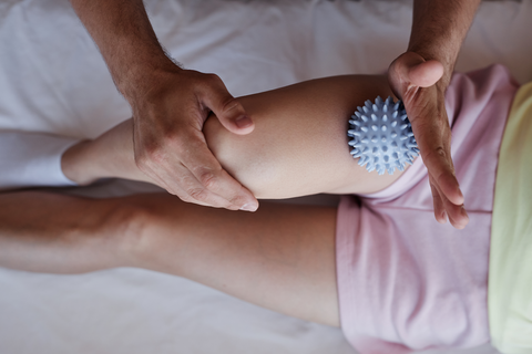 hands treating woman's thigh with bule spiky massage ball