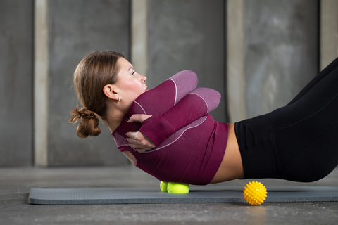 woman laying down on yoga mat with massage ball under back