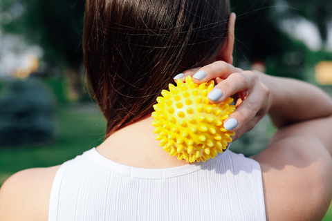 woman using yellow spiky massage ball behind neck