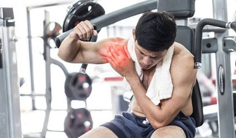 man in gym holding sore shoulder muscle