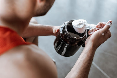 man putting supplement powder in drink in gym