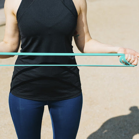 A lady holding a green band at waist height using her arms to pull the band outwards