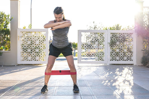 A lady doing banded ankle jumping jacks with a booty band under her knees