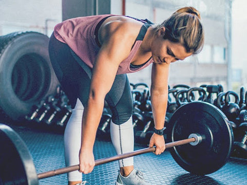 woman bending over about to lift heavy weights in gym beginner