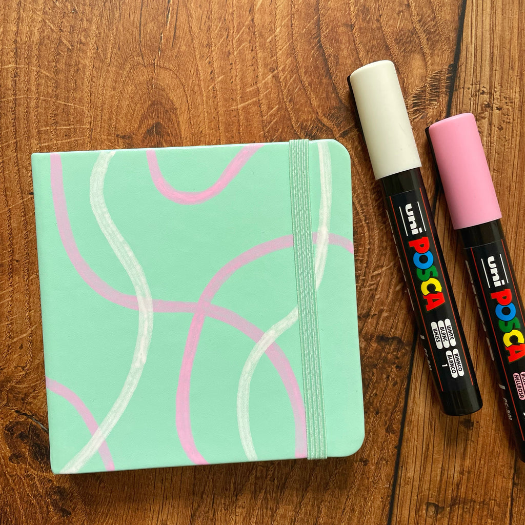 posca paint pens used to decorate a Royal Talens mini square sketchbook with pink and white squiggle pattern