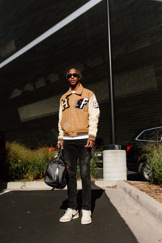 Minnesota Vikings Cornerback, Cameron Dantzler seen wearing the Homme Femme World Champs Letterman Jacket in camel brown. Cream leather contrast sleeves with brown ribbing at cuff and waistband. "HF" patches at front with embroidered "Maison De Homme Femme" at right lower front coincide with the raw racing aesthetic. "World Champs" embroidery at back. 5-button closure at front with 2-button closure at waistband. Welt pockets at front. (via Cameron Dantzler, @camdantzler3)