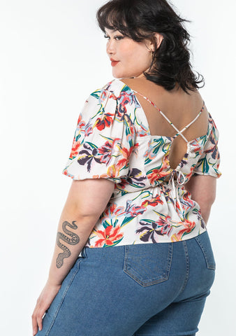An extra large sized model wearing a bohemian white puff sleeve top in a tropical floral print with a sexy back cut out.