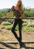 [Color: Black/Fuchsia] A front facing image of a blonde model standing outside wearing a bohemian spring top in a black and pink floral print. With short puff sleeves, a square neckline, and a relaxed fit.