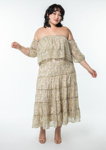 An extra large sized model wearing a light green paisley print maxi dress in sheer chiffon with an off shoulder detail.
