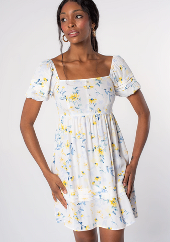 A model wearing a white puff sleeve mini dress with blue and yellow floral details.