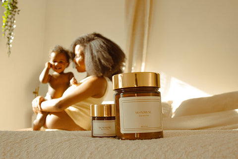 A woman holding her baby with skin muse jars of moisturizer in the foreground