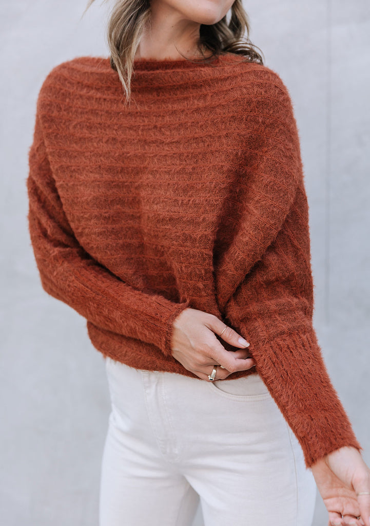 [Color: Burnt Orange] A blonde model wearing a fuzzy dark orange boatneck sweater. The wide neckline can be worn off the shoulder.  