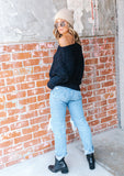 [Color: Black] A blonde model wearing a fuzzy black boatneck sweater. The wide neckline can be worn off the shoulder.  