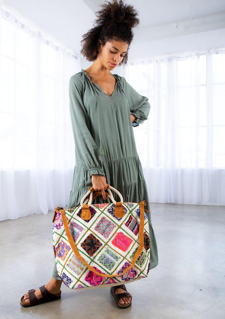 [Color: Multi/Natural] A model holding a patchwork weekender bag. With embroidered details, suede trim, suede top handles, and a suede long adjustable strap.