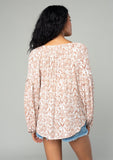 [Color: Ivory/Sand] A back facing image of a brunette model wearing a best selling billowy resort blouse in an ivory and sand bohemian diamond print. With exaggerated long sleeves and a split v neckline with tassel ties. 