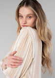 [Color: Natural/Tan] A close up side facing image of a blonde model wearing a resort ready bohemian top in a natural and tan stripe. With long sleeves, a v neckline, and a tie front waist. 