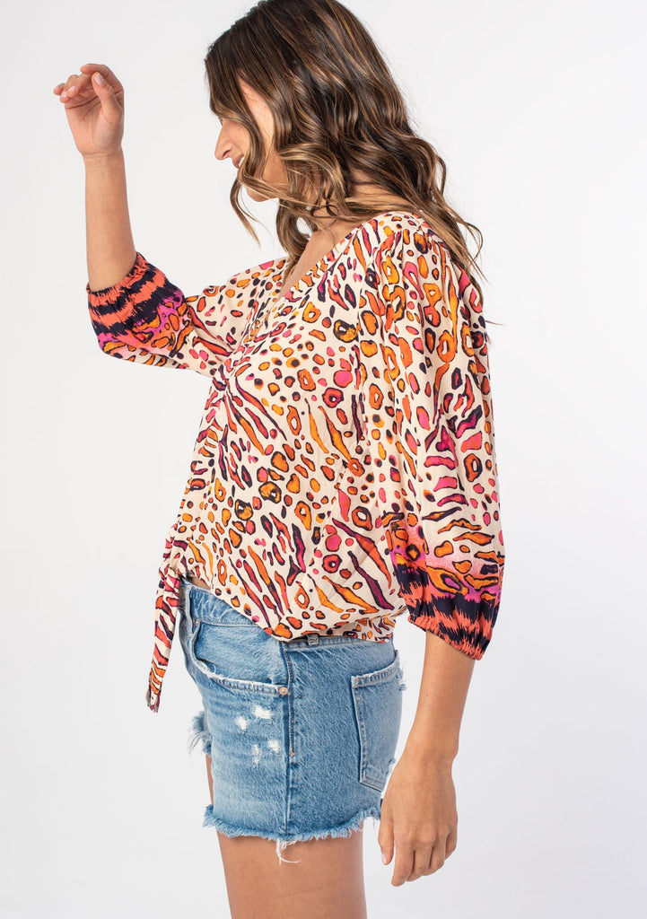 [Color: Natural/Fuchsia] A woman wearing a natural and pink abstract leopard print top with long sleeves and a tie front detail. 