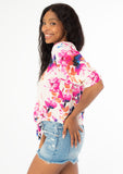 [Color: Ivory/Fuchsia] A side facing image of a black model wearing a pink and white watercolor floral print top with a tie front waist detail, half length sleeves, and a v neckline. 