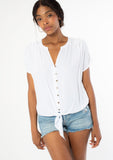 [Color: Chalk] A front facing image of a black model wearing a soft and silky white short sleeve top with a button front and tie waist detail. 