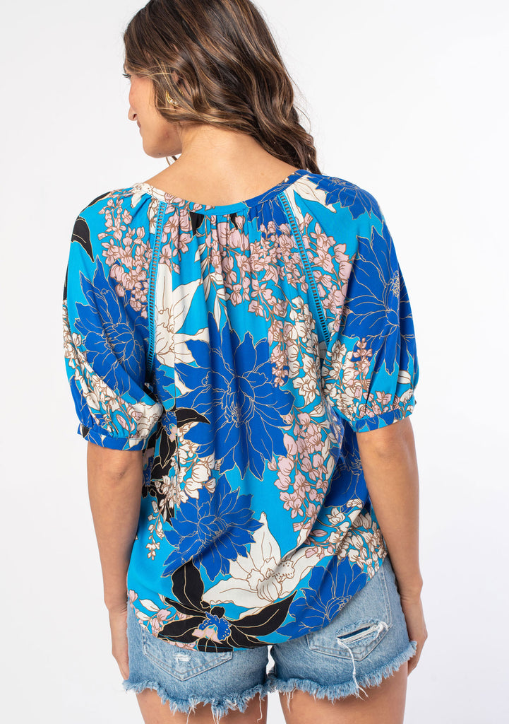 [Color: Turquoise/Black] A woman wearing a flowy bohemian top in a blue and black large floral print. With half length puff sleeves and a button front. 