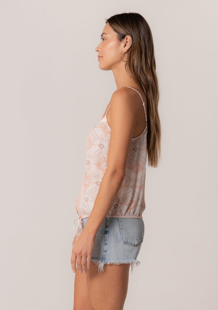 [Color: Natural/Peach] A side facing image of a brunette model wearing a summer tank top in a pink bohemian print. With adjustable spaghetti straps, a scoop neckline, a button front, a drawstring waist with tassel ties, and a relaxed fit. 