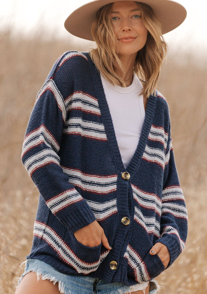 [Color: Navy/Sky] A model wearing a navy blue stripe cardigan sweater. With three oversize buttons, front pockets, and a v neckline. 