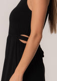 [Color: Black] A close up side facing image of a brunette model wearing a soft and stretchy knit sleeveless maxi dress in black. With a v neckline, sexy side waist cutouts, and a self tie belt. 