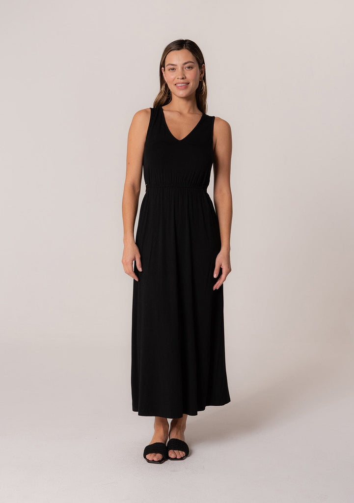 [Color: Black] A front facing image of a brunette model wearing a soft and stretchy knit sleeveless maxi dress in black. With a v neckline, sexy side waist cutouts, and a self tie belt. 