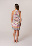 [Color: Natural/Yellow] A back facing image of a brunette model wearing a casual bohemian summer mini dress in a mixed floral print. A sleeveless dress with a racerback, a smocked elastic waist, a split v neckline with tassel ties, and a relaxed fit. 