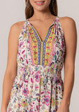 [Color: Natural/Yellow] A close up front facing image of a brunette model wearing a casual bohemian summer mini dress in a mixed floral print. A sleeveless dress with a racerback, a smocked elastic waist, a split v neckline with tassel ties, and a relaxed fit. 