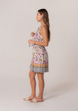 [Color: Natural/Yellow] A side facing image of a brunette model wearing a casual bohemian summer mini dress in a mixed floral print. A sleeveless dress with a racerback, a smocked elastic waist, a split v neckline with tassel ties, and a relaxed fit. 