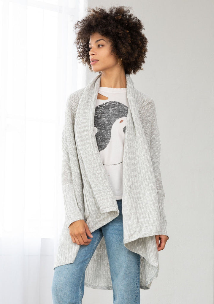 [Color: Silver/Ivory] A model wearing a silver grey knit reversible cardigan. With long sleeves, a waterfall open front, side pockets, and a shawl collar. 