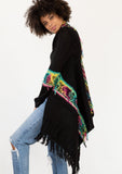 [Color: Black/Multi] A model wearing a black chunky knit cardigan with a multicolor shaggy yarn detail. Featuring a fringed waterfall hemline and an open front.