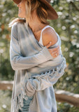 [Color: Chambray/Offwhite] A model wearing a light blue and off white space dye stripe sweater. With a side button closure, long sleeves, and a fringed waterfall hemline. 