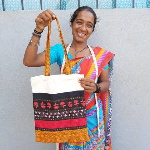 image of a smiling Shakti.ism artisan in Pondicherry, holding up a bright coloured upcycled sari and cotton tote bag