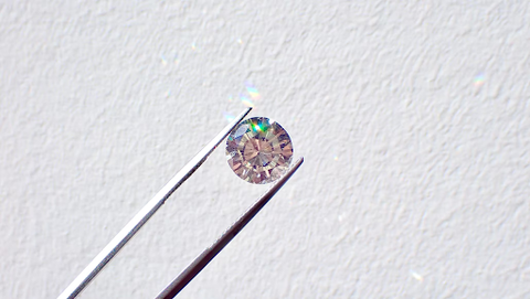 A diamond held in a pair of needle-nose jewelry pliers.