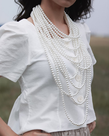 Model wearing layers of pearl necklaces.