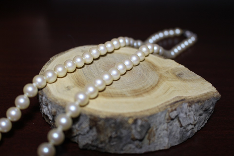 a pearl necklace strewn over a slab of white wood against a dark background