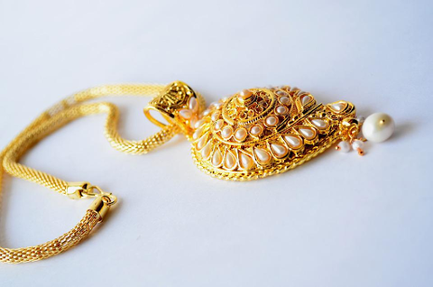 a gold necklace with a large pendant curled on a white table